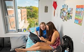 Two students sitting on a bed in a their room in the Greiner Hall residence hall. 