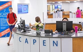 1 Capen reception desk with a student walking by on the left side. 