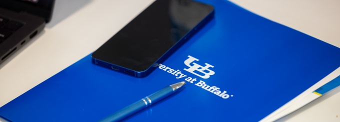 University at Buffalo folder, smartphone and pen on a desk. 