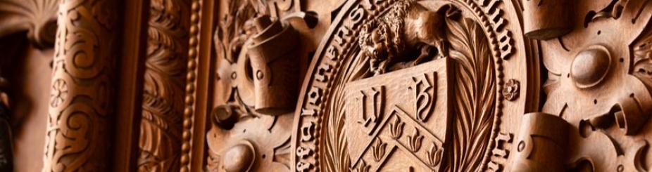 Intricately carved wooden panel featuring the University at Buffalo seal with the UB logo and Latin inscription.