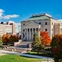 Building with columns in front with fall trees and a blue sky. 