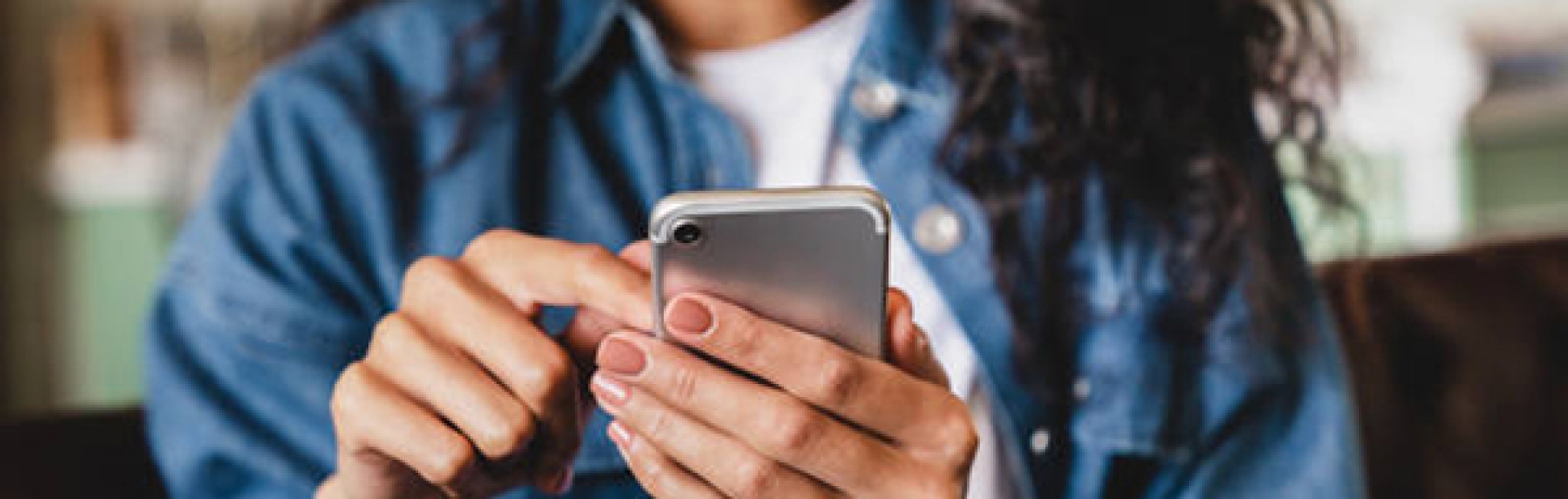 Female student in a denim jacket using a smartphone, seated indoors. 
