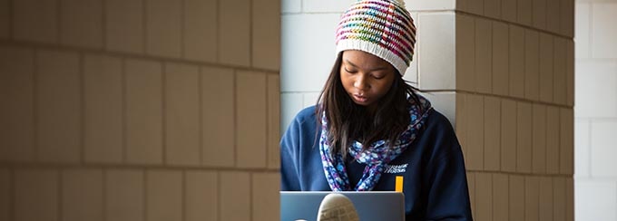 Student sitting on interior window ledge with laptop. 
